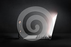 Businessman stands front of an open glowing huge laptop in the darkness. Profile view.