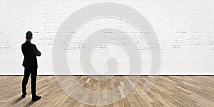 Businessman stands opposite bricks wall in gallery interior with wooden floor