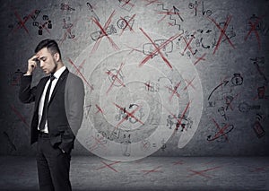 Businessman stands pondering on the concrete background with depicted ideas that crossed by red
