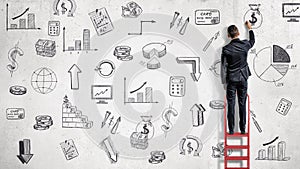 A businessman stands on a red ladder and draws financial illustrations on a while wall.
