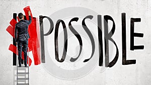 A businessman stands on a stepladder and hides the word Impossible written on the wall using a red paint roller.