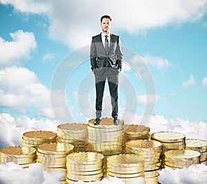 Businessman staying on pile of gold coins on the clouds t blue s