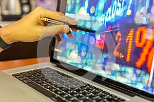 Businessman stock analysis hand with pen pointing on laptop screen financial chart graph in background.