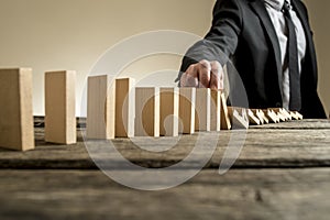 Businessman stopping domino effect with his finger