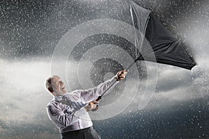 Businessman struggling to keep hold of inside-out umbrella in storm