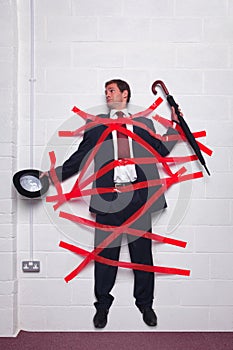 Businessman stuck to wall with red tape