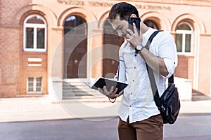 Businessman or student on background of city. Young man in white shirt talking on phone outdoors