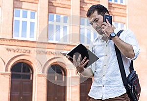 Businessman or student on background of city. Young man in white shirt talking on phone outdoors