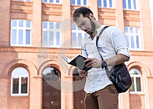 Businessman or student on background of city. Young man in white shirt talking on phone outdoors