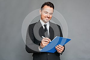 Businessman studio standing isolated on grey with clipboard taking notes smiling joyful