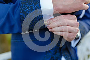 Businessman in a stylish blue suit with patterns adjusts the cuffs of his shirt. Stylish man in an expensive suit and tie and