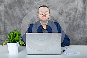 Businessman in stylish blue suit using laptop next to a green plant in modern office environment