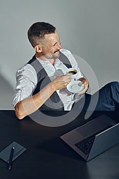 Businessman with stylish mustache, dressed in classic suit is smiling, looking away while sitting at table in office and