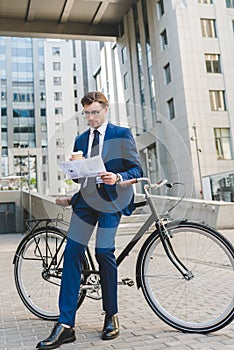 businessman in stylish suit with newspaper and paper cup of coffee leaning