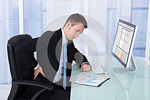 Businessman suffering from backache at computer desk photo