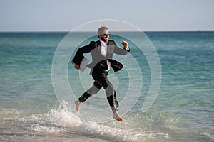 Businessman suit barefoot running on beach. Handsome business man on summer vacation. Businessman running on sea holding
