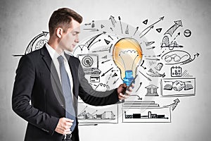 Businessman in suit is browsing internet via smartphone, find new ideas for start up. Colorful light bulb sketch and business