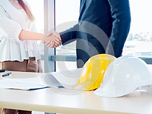 Businessman in suit, engineering or architect and woman shaking hands on blueprint and yellow and white safety hard hat on desk