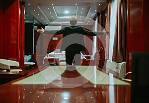 A businessman in a suit with his arms outstretched, photographed from behind in his hotel room. The sky is the limit