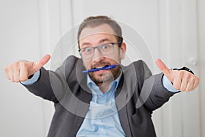Businessman in suit holding ballpoint pen with his teeth and giving thumbs up