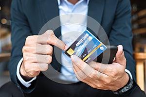 Businessman in suit holding credit card and using touchscreen smartphone for online shopping while making orders in the cafe or