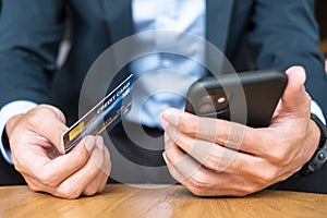 Businessman in suit holding credit card and using touchscreen smartphone for online shopping while making orders in the cafe or