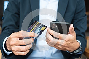 Businessman in suit holding credit card and using touchscreen smartphone for online shopping while making orders in the cafe or