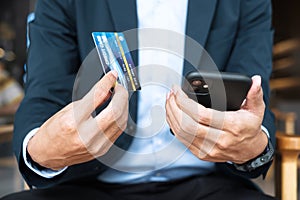 Businessman in suit holding credit card and using touchscreen smartphone for online shopping while making orders in the cafe or