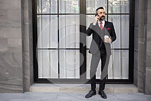 Businessman in Suit Holding a Cup of Coffee While Talking on His Mobile Phone