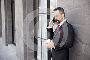 Businessman in Suit Holding a Cup of Coffee While Talking on His Mobile Phone