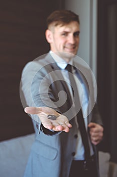 Businessman in suit holding house key in hand. Mortgage, credit or property concept