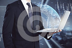 Businessman in a suit holding a laptop with a hologram globe in the background. International and worldwide communication concept