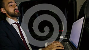 Businessman in suit looking over the windown of his limousine and typing on