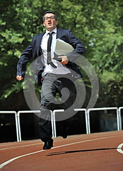 Businessman in suit and necktie carrying folder running desperate in stress on athletic track