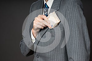 Businessman in suit putting banknotes in his jacket breast pocket. Business man is holding cash, stack of fifty euros money. Pers