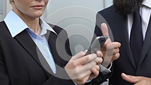 Businessman in suit scolding female secretary scrolling phone outdoor, deadline