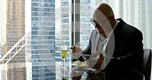 Businessman in a suit, he sits in his office`s panoramic window in which you can see high-rise buildings, round glass