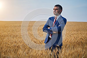 businessman in a suit stands in a field of ripe wheat and looks into