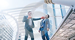 Businessman in suit uniform wearing boxing gloves and punching business man`s face