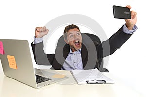 Businessman in suit working at office laptop computer desk using mobile phone for taking selfie photo