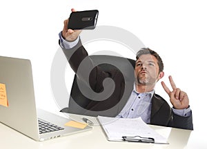 Businessman in suit working at office laptop computer desk using mobile phone for taking selfie photo