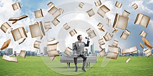 Businessman in summer park announcing something in loudspeaker and books falling from above