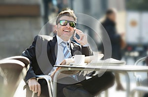 Businessman in sunglasses having breakfast coffee early morning reading newspaper news talking on mobile phone