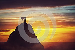 Businessman superhero conceptual scene. Determined hero with red cape stands brave on a mountain peak. Business leadership,