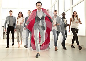 Businessman in a superhero`s cloak is ahead of the business team