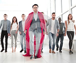 Businessman in a superhero`s cloak is ahead of the business team