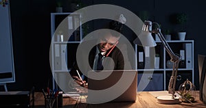 Businessman taking notes while talking on mobile phone at night office