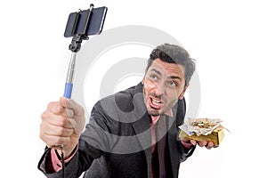 Businessman taking selfie photo with mobile phone camera and stick posing happy and successful with gold bar and money