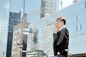 Businessman talking on cell phone on background modern office corporate buildings