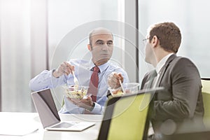 Businessman talking with colleague while eating lunch in boardroom during meeting at office